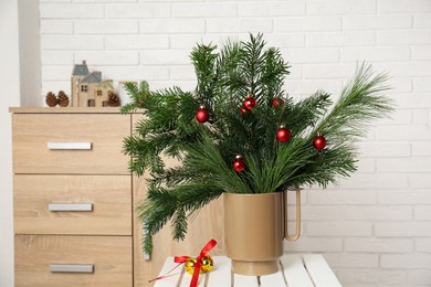 Photo of Beautiful Christmas composition of decorated fir and pine tree branches on stool at home