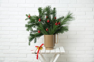 Photo of Beautiful Christmas composition of decorated fir and pine tree branches on stool near white brick wall