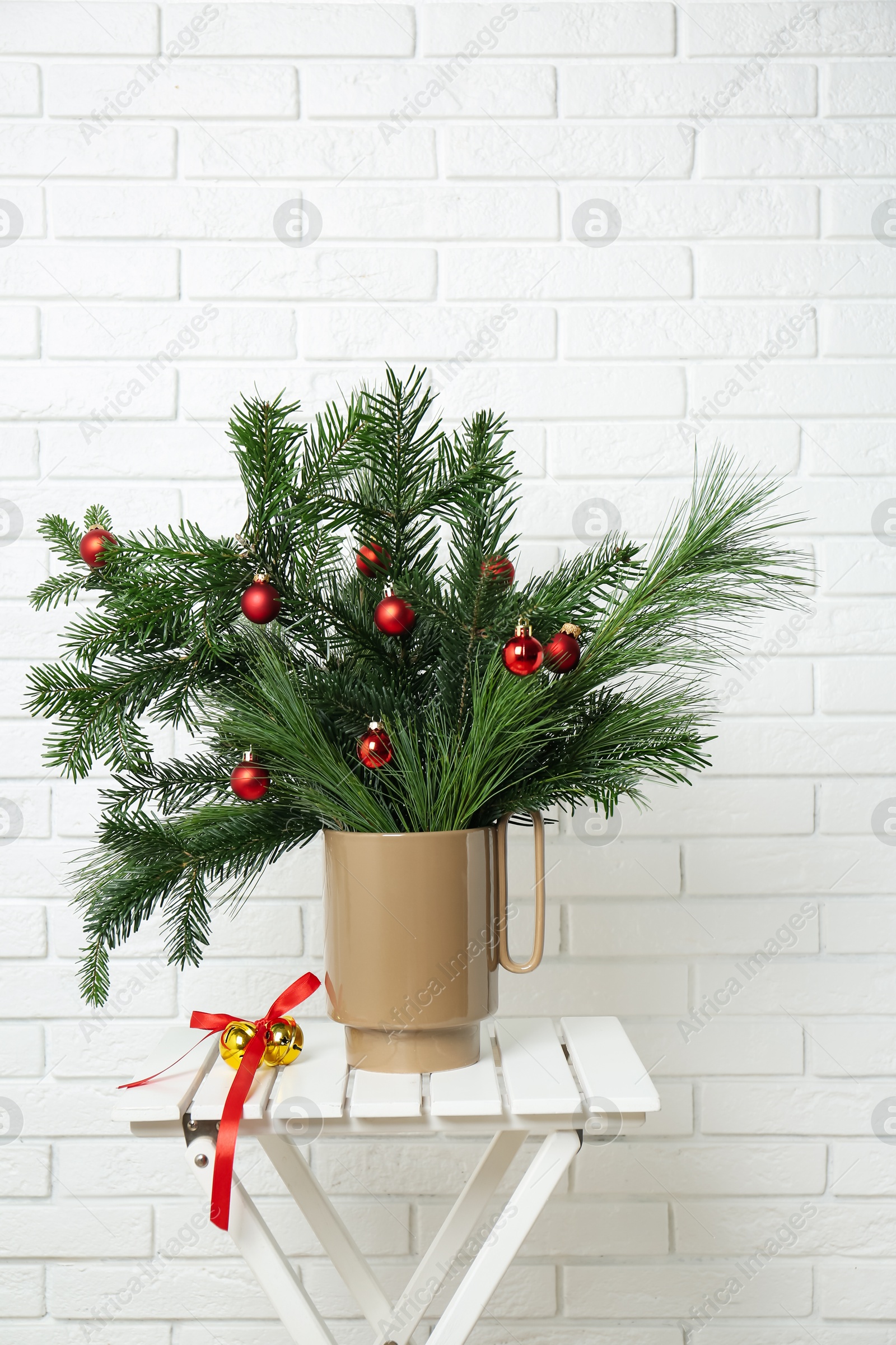 Photo of Beautiful Christmas composition of decorated fir and pine tree branches on stool near white brick wall