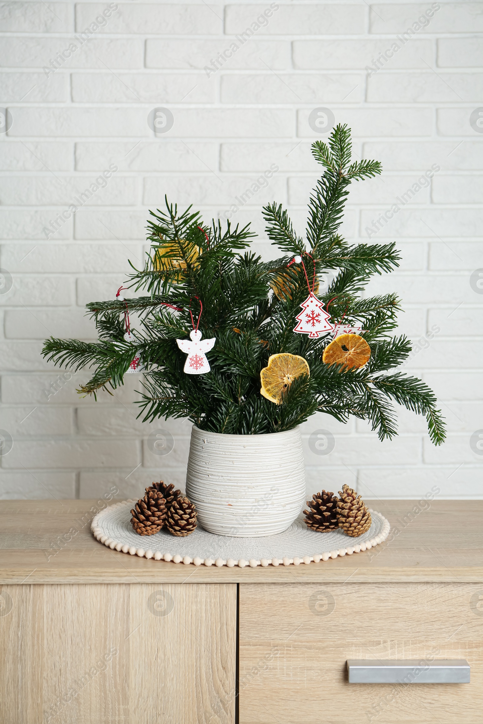 Photo of Beautiful Christmas composition of decorated fir tree branches on wooden nightstand near white brick wall