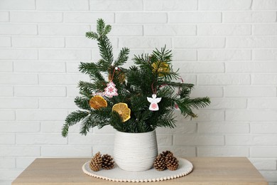 Photo of Beautiful Christmas composition of decorated fir tree branches on wooden table near white brick wall