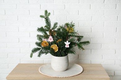 Photo of Beautiful Christmas composition of decorated fir tree branches on wooden table near white brick wall