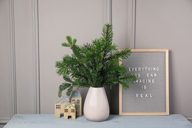 Photo of Fir tree branches in vase and mood board on gray wooden table indoors. Christmas decor