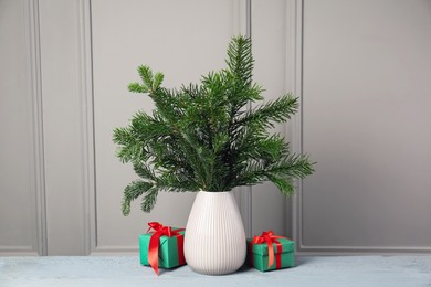 Photo of Fir tree branches in vase and Christmas gifts on gray wooden table indoors