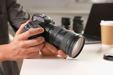 Photo of Photographer with professional camera at white desk indoors, closeup