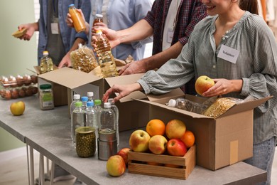 Photo of Group of volunteers packing food donations at table indoors, closeup