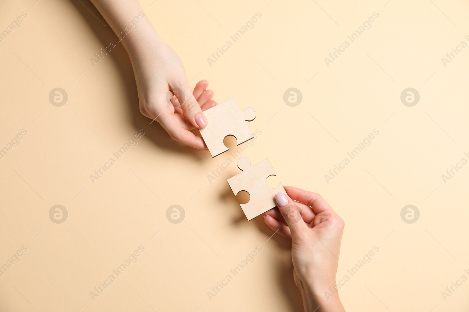 Photo of Business strategy and teamwork concept. Partners putting puzzle pieces together on beige background, top view