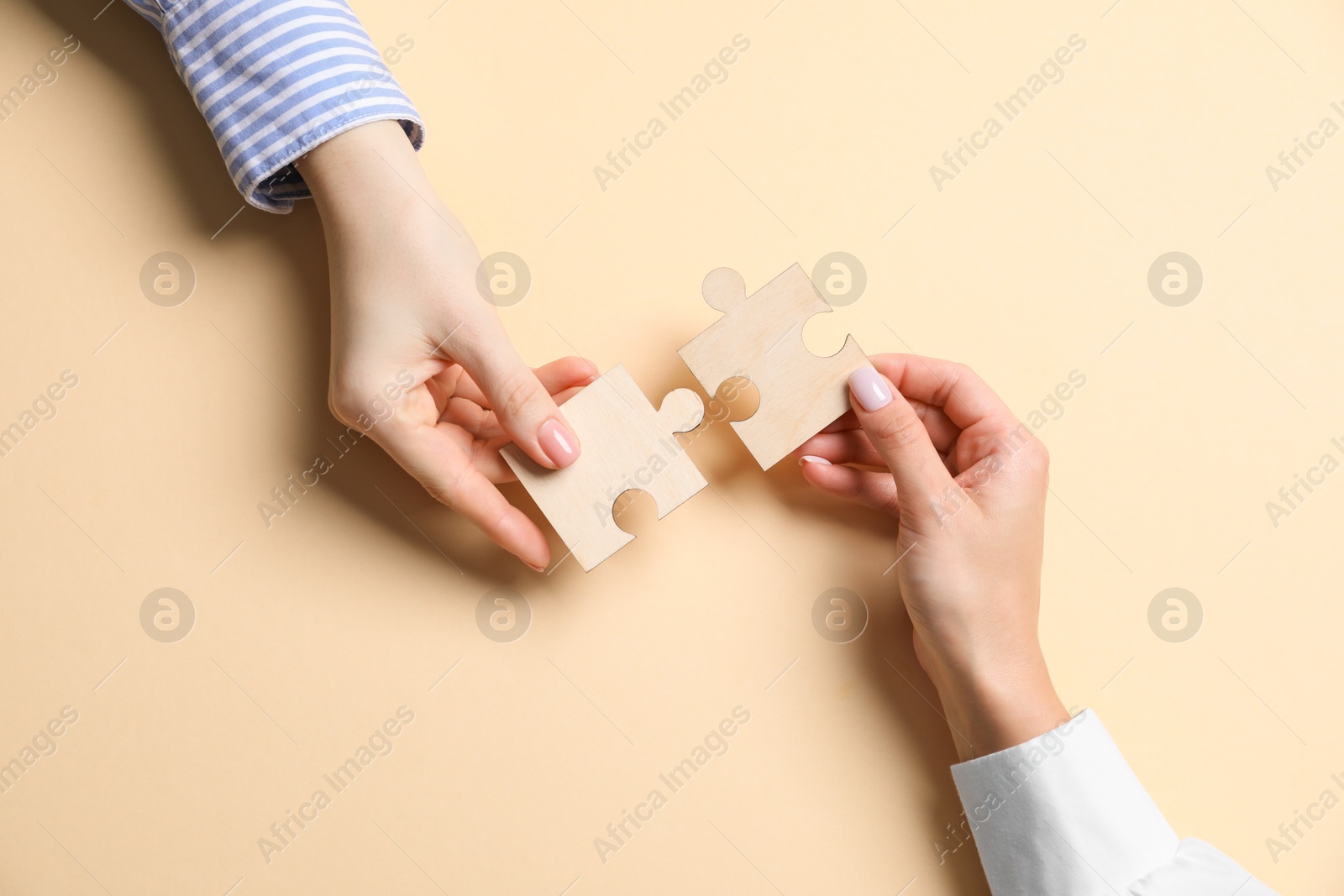 Photo of Business strategy and teamwork concept. Partners putting puzzle pieces together on beige background, top view