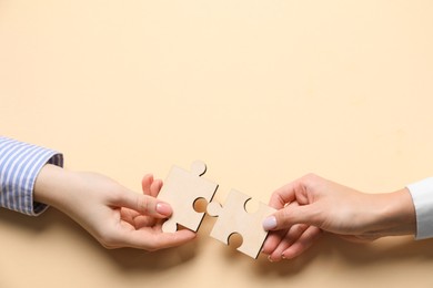 Photo of Business strategy and teamwork concept. Partners putting puzzle pieces together on beige background, top view. Space for text