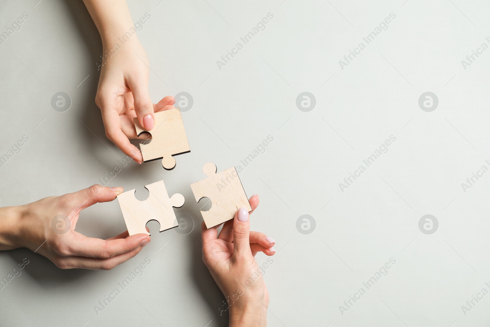 Photo of Business strategy and teamwork concept. Partners with different puzzle pieces on grey background, top view. Space for text