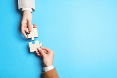 Photo of Business strategy and teamwork concept. Partners putting puzzle pieces together on light blue background, top view. Space for text