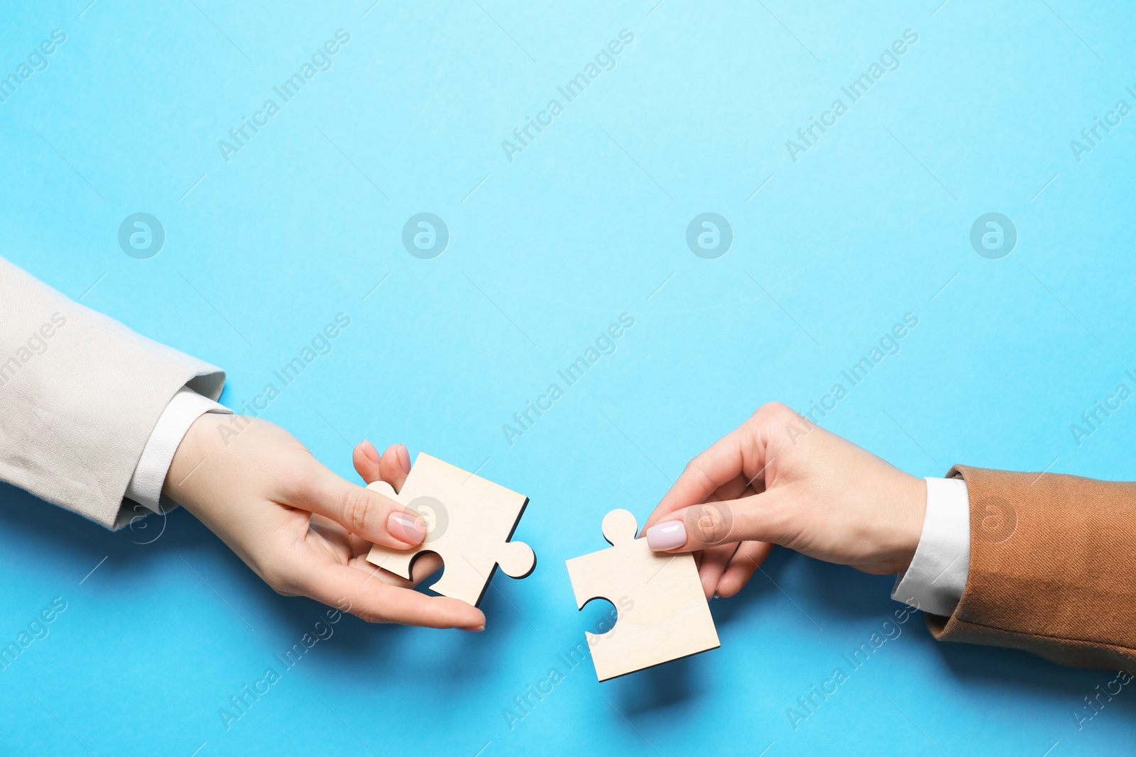 Photo of Business strategy and teamwork concept. Partners putting puzzle pieces together on light blue background, top view. Space for text