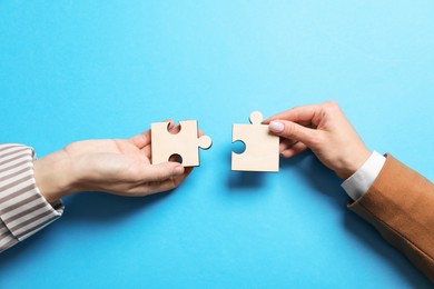 Photo of Business strategy and teamwork concept. Partners putting puzzle pieces together on light blue background, top view