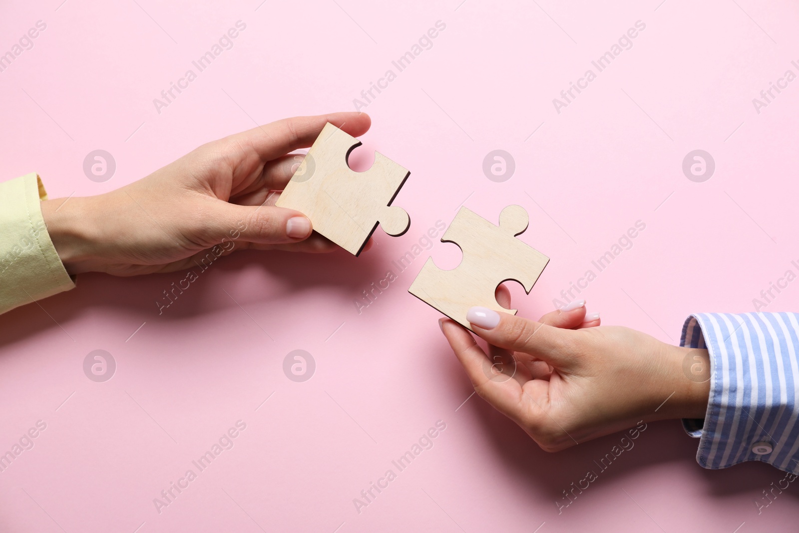 Photo of Business strategy and teamwork concept. Partners putting puzzle pieces together on pink background, top view