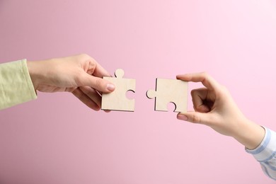 Photo of Business strategy and teamwork concept. Partners putting puzzle pieces together on pink background, closeup