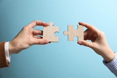 Photo of Business strategy and teamwork concept. Partners putting puzzle pieces together on light blue background, closeup