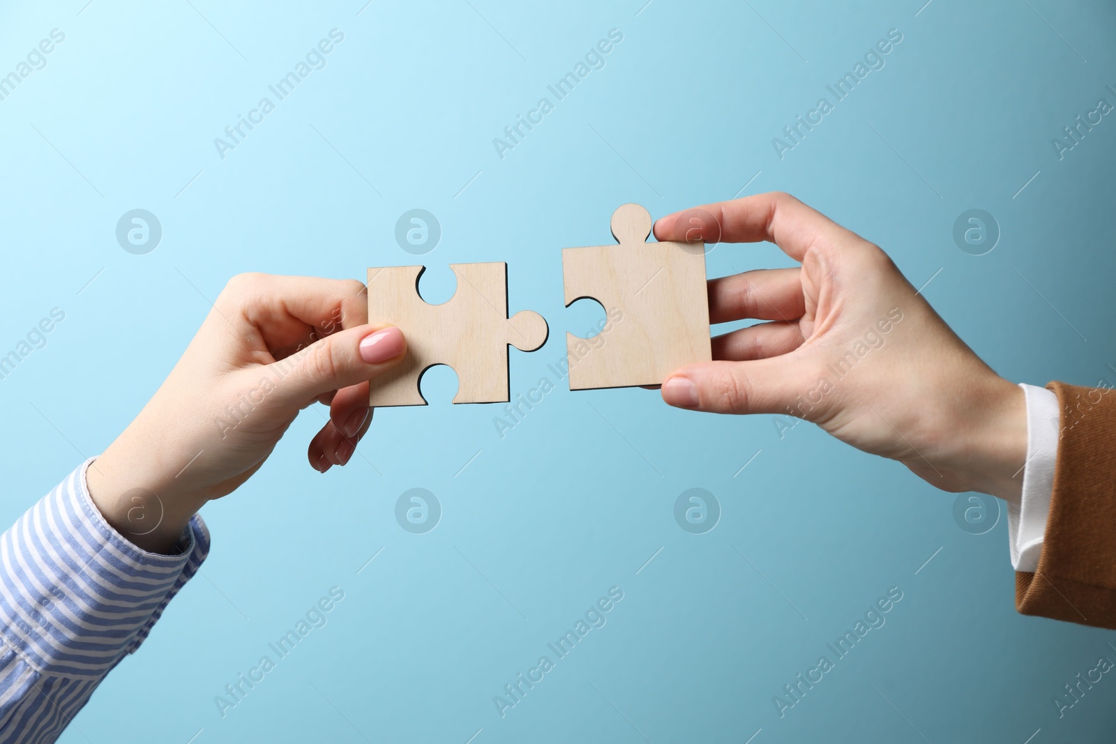 Photo of Business strategy and teamwork concept. Partners putting puzzle pieces together on light blue background, closeup