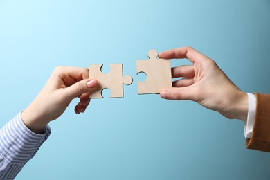 Photo of Business strategy and teamwork concept. Partners putting puzzle pieces together on light blue background, closeup