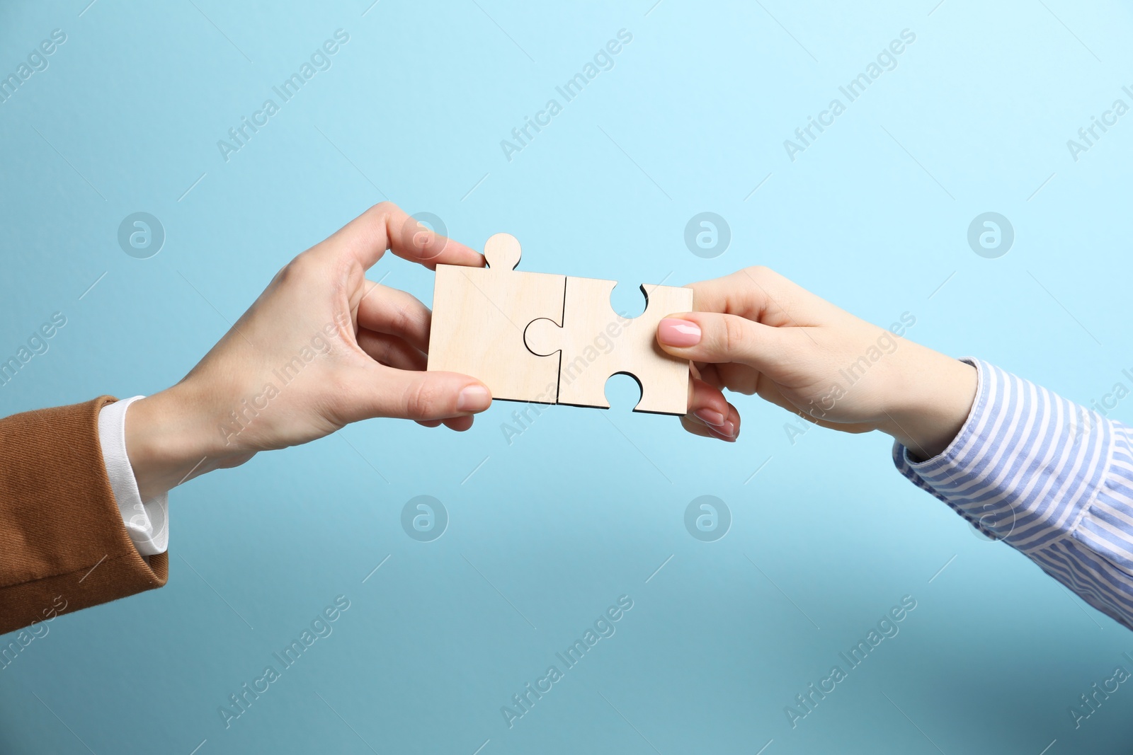 Photo of Business strategy and teamwork concept. Partners putting puzzle pieces together on light blue background, closeup