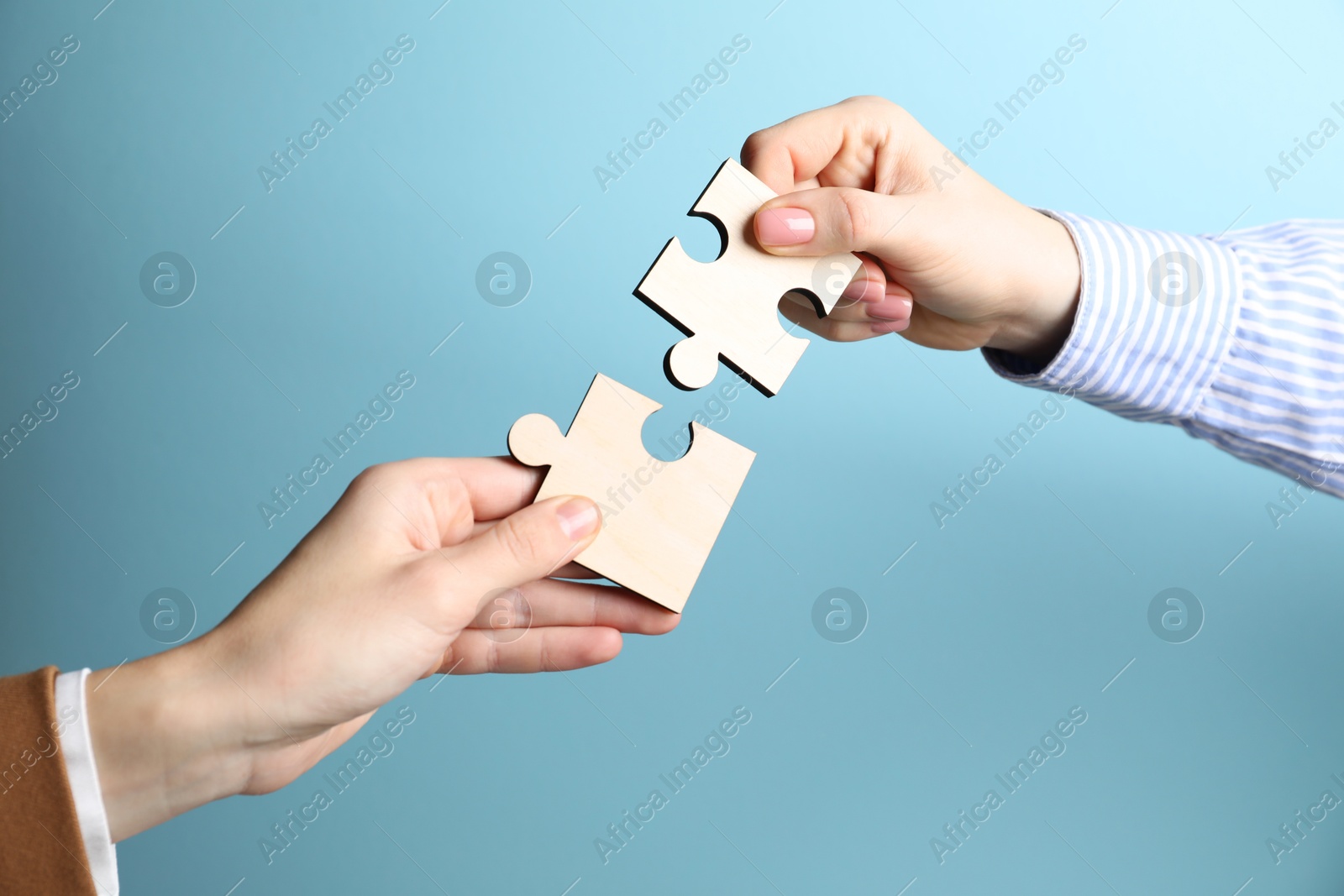 Photo of Business strategy and teamwork concept. Partners putting puzzle pieces together on light blue background, closeup