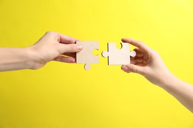 Photo of Business strategy and teamwork concept. Partners putting puzzle pieces together on yellow background, closeup