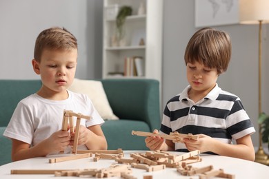 Photo of Cute brothers playing with wooden construction set at table indoors