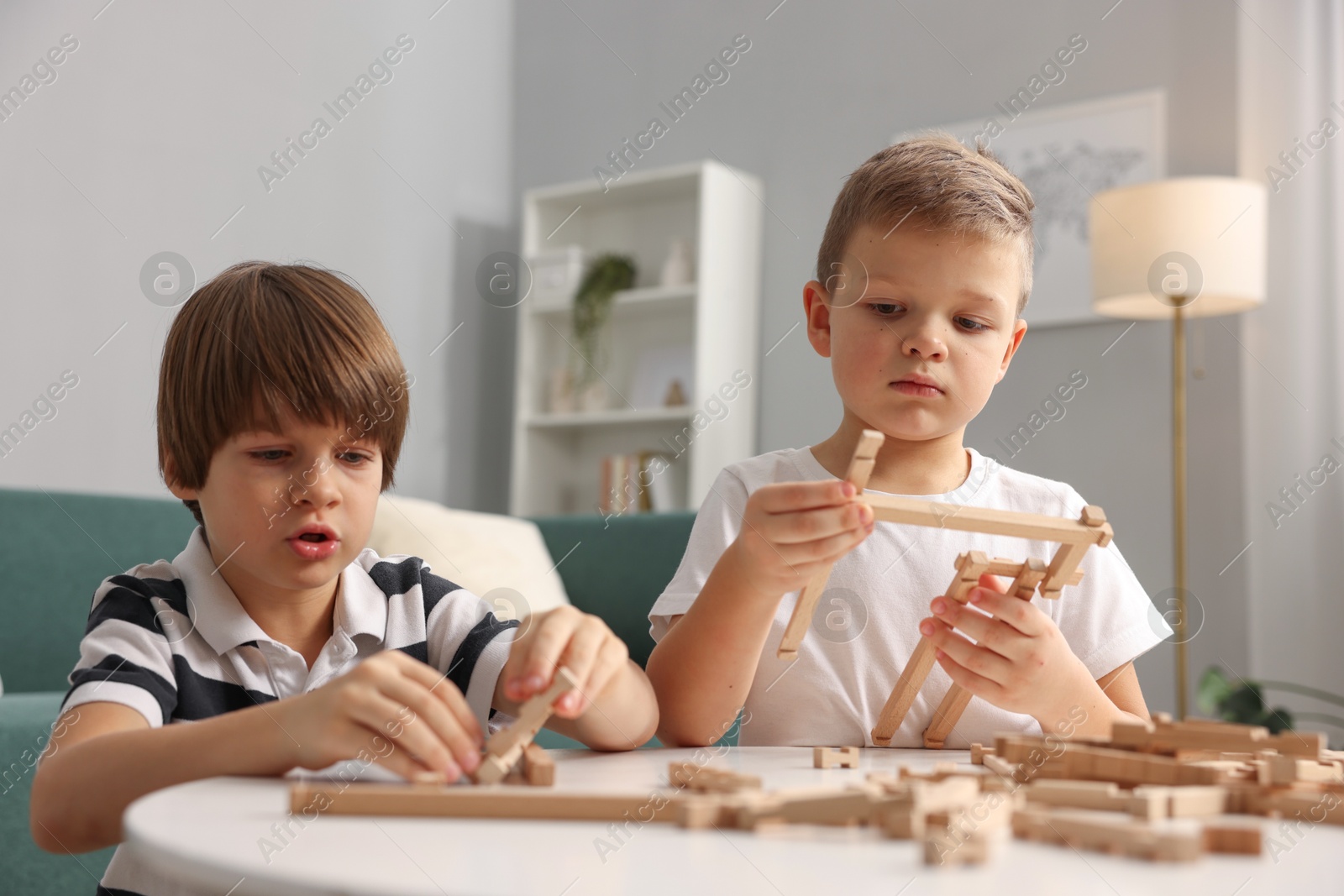 Photo of Cute brothers playing with wooden construction set at table indoors