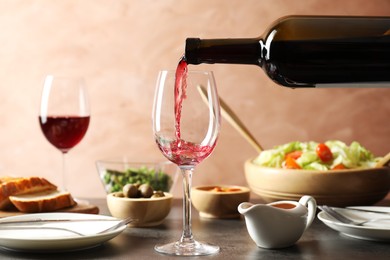 Photo of Pouring red wine into glass at grey table with tasty food, closeup