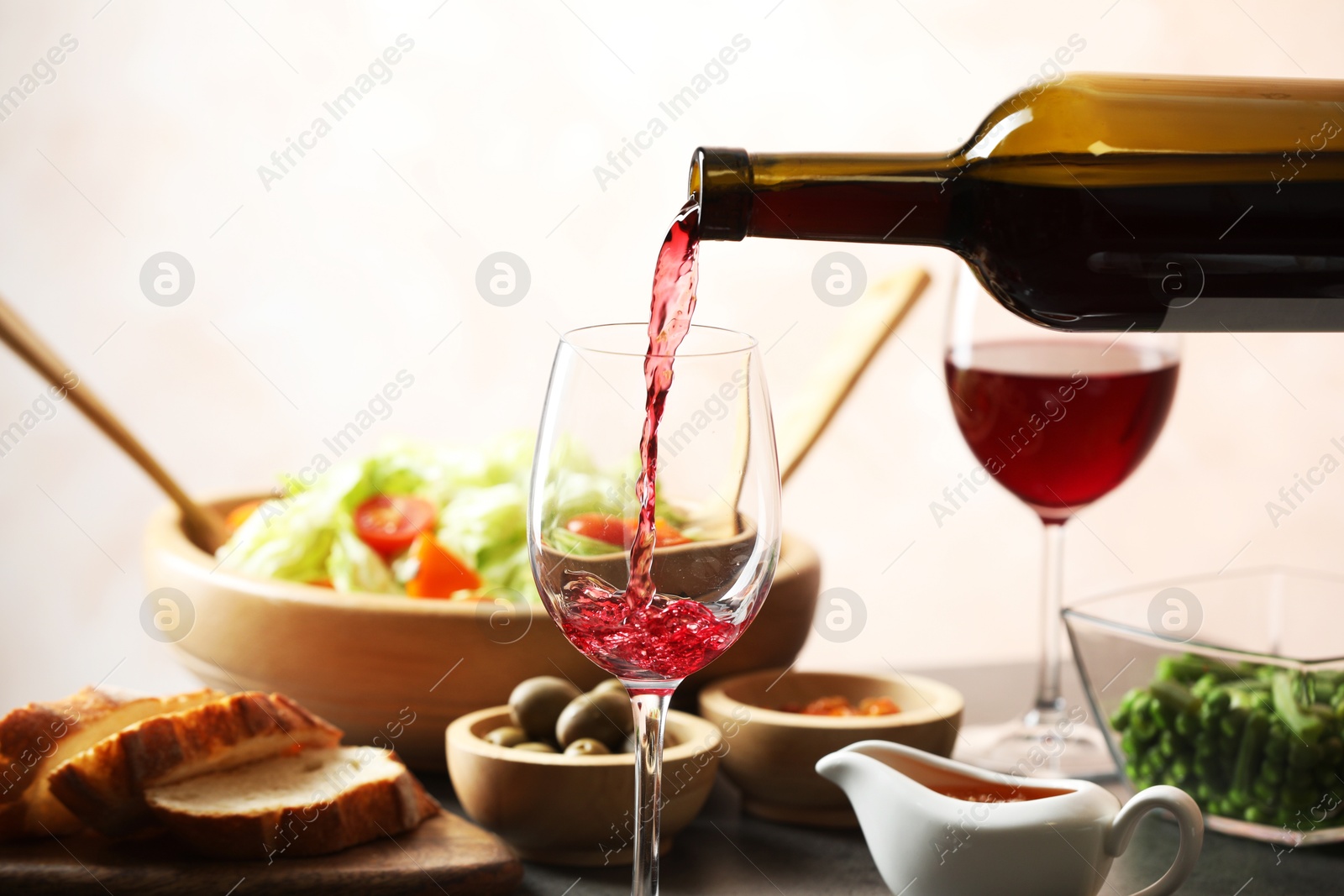 Photo of Pouring red wine into glass at grey table with tasty food, closeup