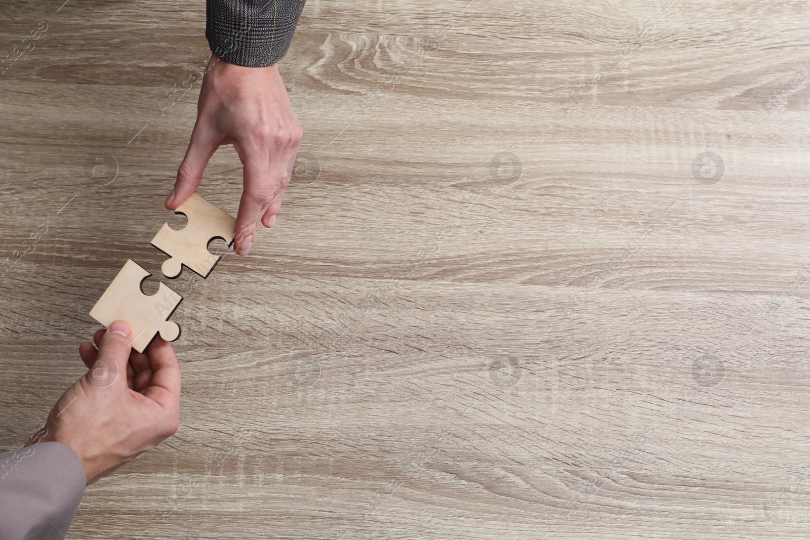 Photo of Teamwork. People putting puzzle pieces together at wooden table, top view. Space for text