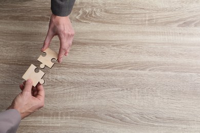 Photo of Teamwork. People putting puzzle pieces together at wooden table, top view. Space for text