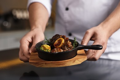 Photo of Professional chef serving dish at table indoors, closeup