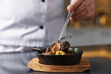 Photo of Professional chef serving dish at table indoors, closeup