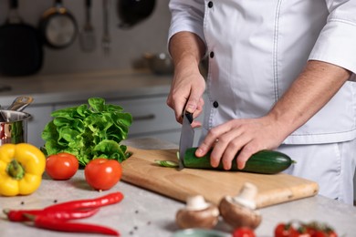 Photo of Professional chef cutting zucchini at table in kitchen, closeup