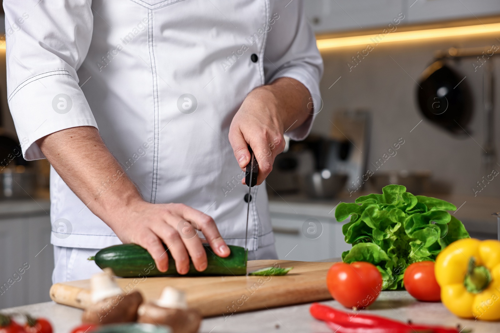 Photo of Professional chef cutting zucchini at table in kitchen, closeup