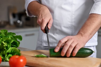 Photo of Professional chef cutting zucchini at table in kitchen, closeup