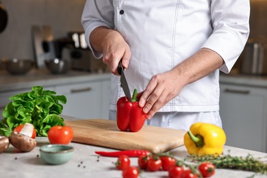 Photo of Professional chef cutting bell pepper at table in kitchen, closeup