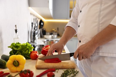 Photo of Professional chef cutting bell pepper at counter in kitchen, closeup