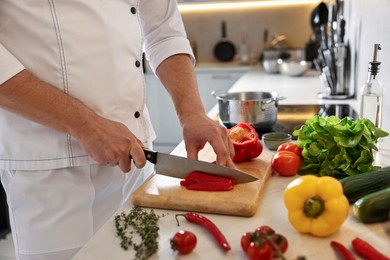 Photo of Professional chef cutting bell pepper at counter in kitchen, closeup