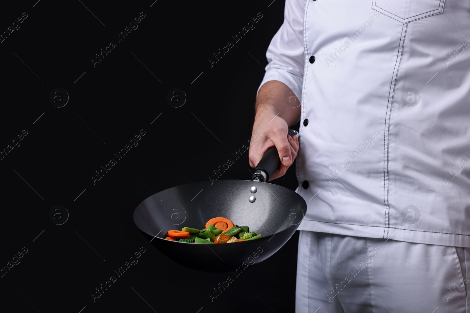 Photo of Professional chef mixing vegetables in wok on black background, closeup. Space for text