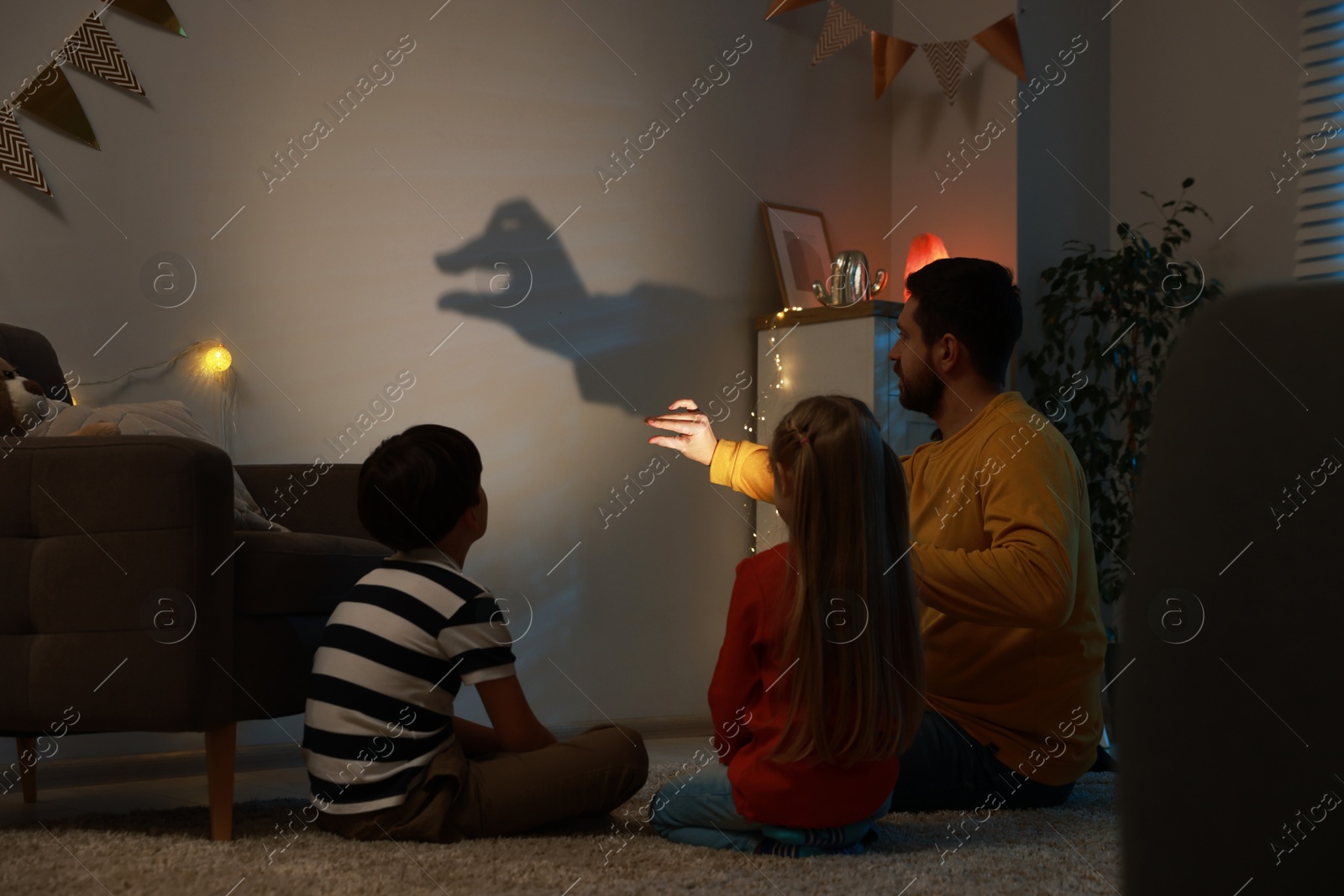 Photo of Man making hand gesture like goose while performing shadow play to his kids at home