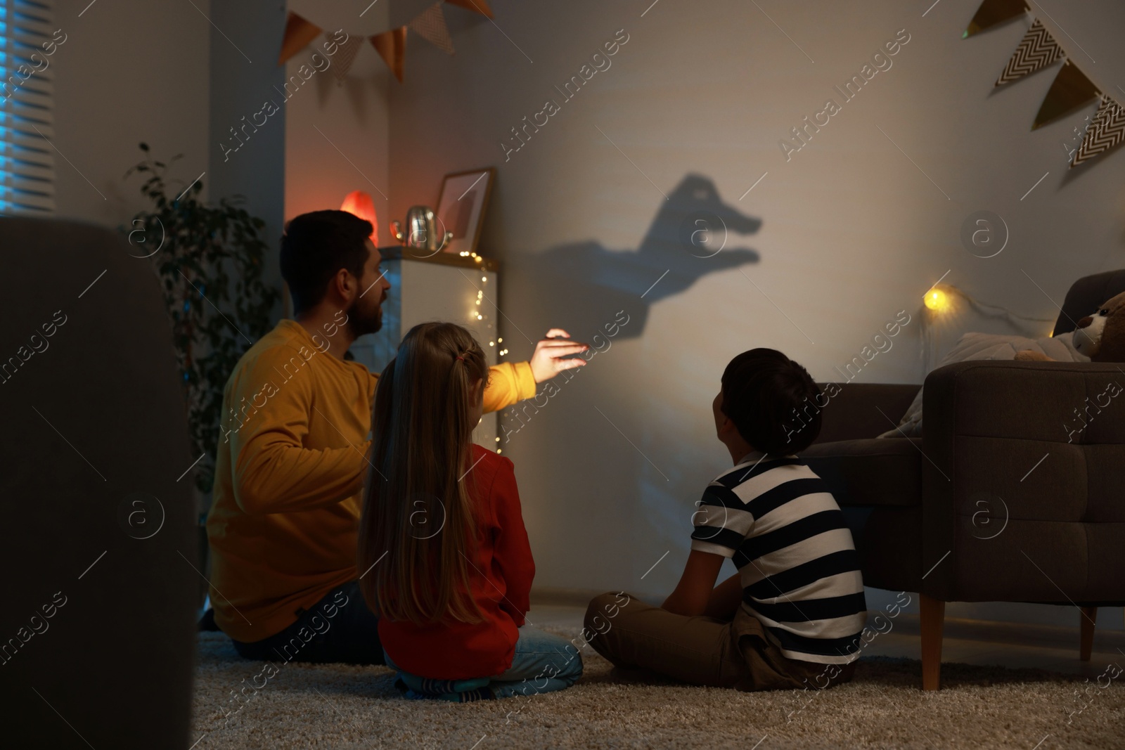 Photo of Man making hand gesture like goose while performing shadow play to his kids at home