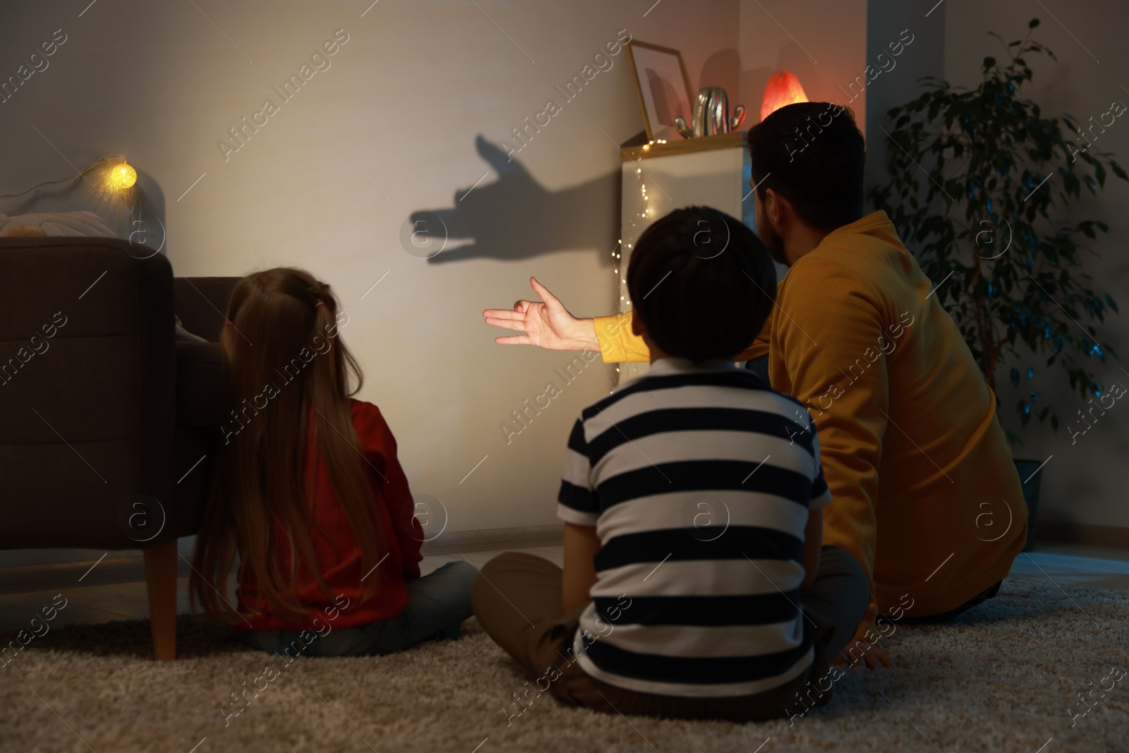 Photo of Man making hand gesture like dog while performing shadow play to his kids at home, back view