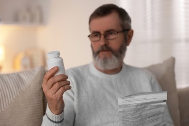 Photo of Senior man with bottle of pills and instruction at home, selective focus