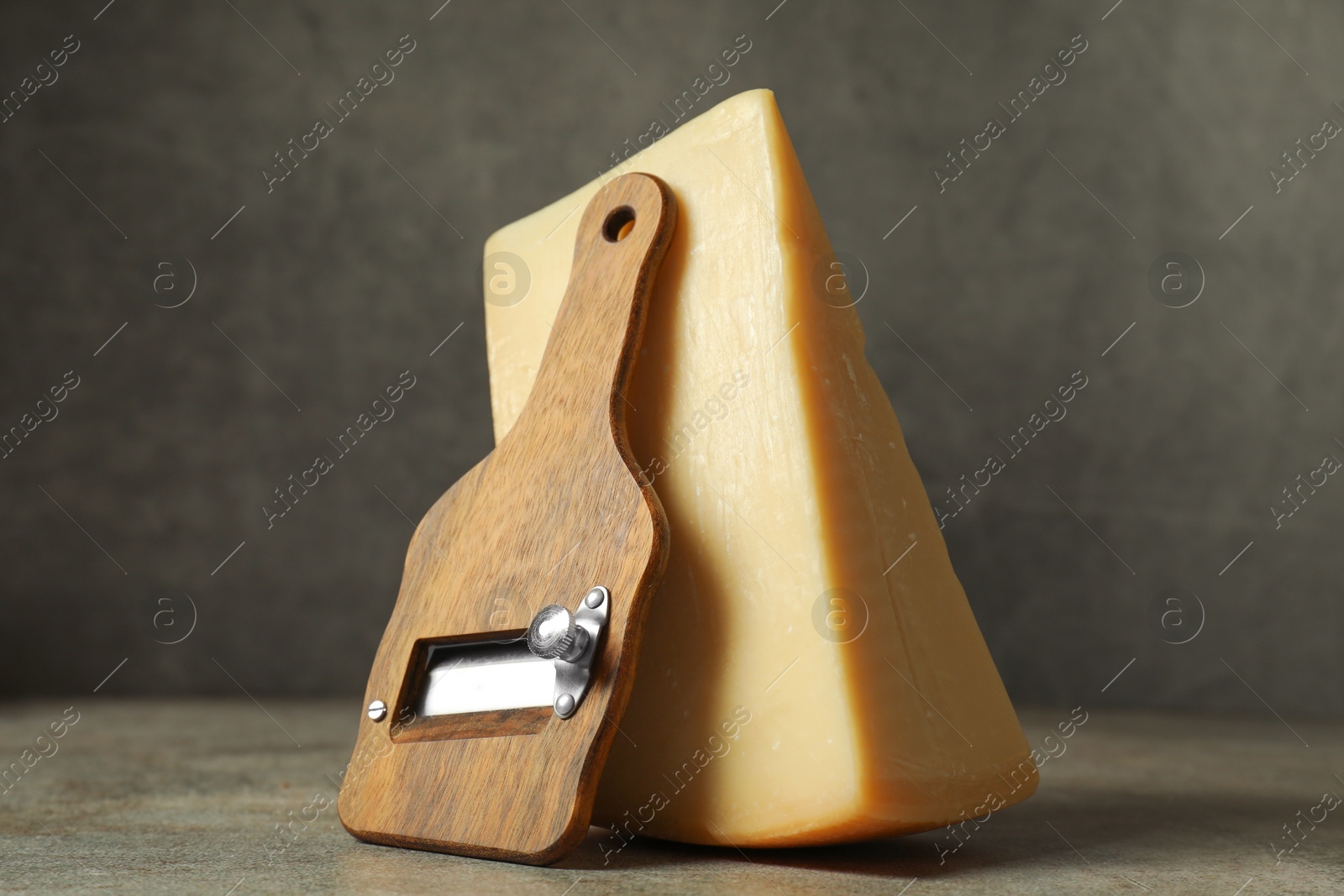 Photo of Piece of tasty cheese and slicer on grey table, closeup