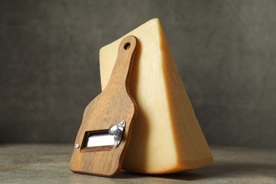 Photo of Piece of tasty cheese and slicer on grey table, closeup