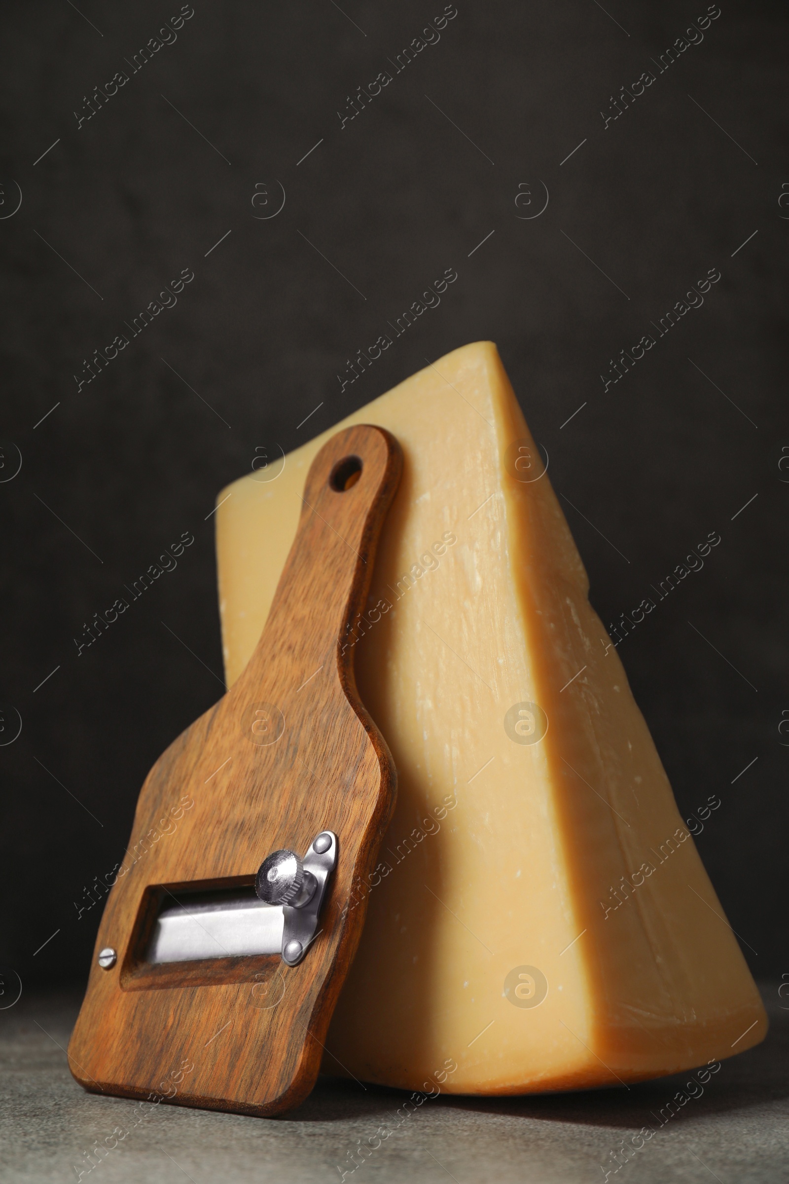 Photo of Piece of tasty cheese and slicer on grey table, closeup