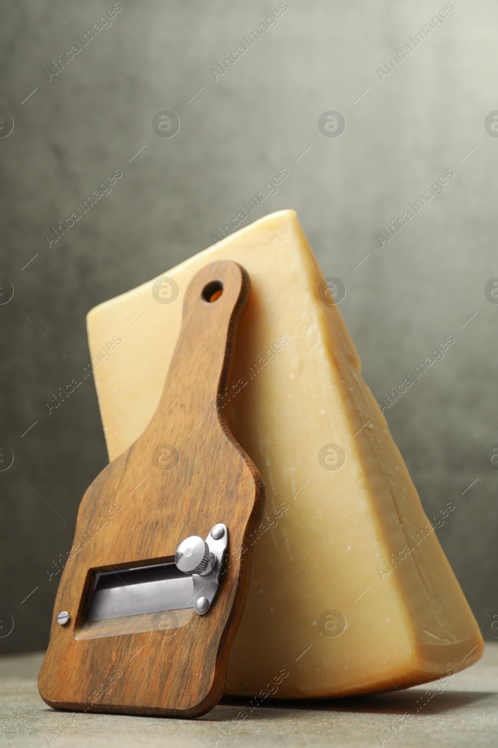 Photo of Piece of tasty cheese and slicer on grey table, closeup