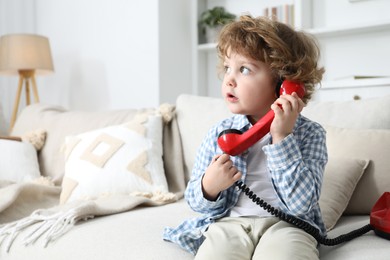 Photo of Cute little boy with telephone on sofa indoors