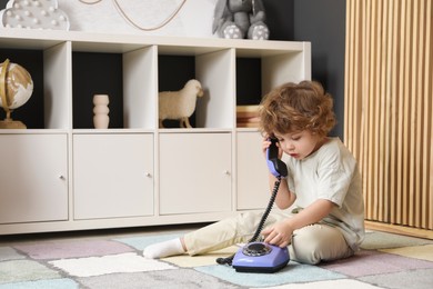 Photo of Cute little boy with telephone on floor indoors, space for text